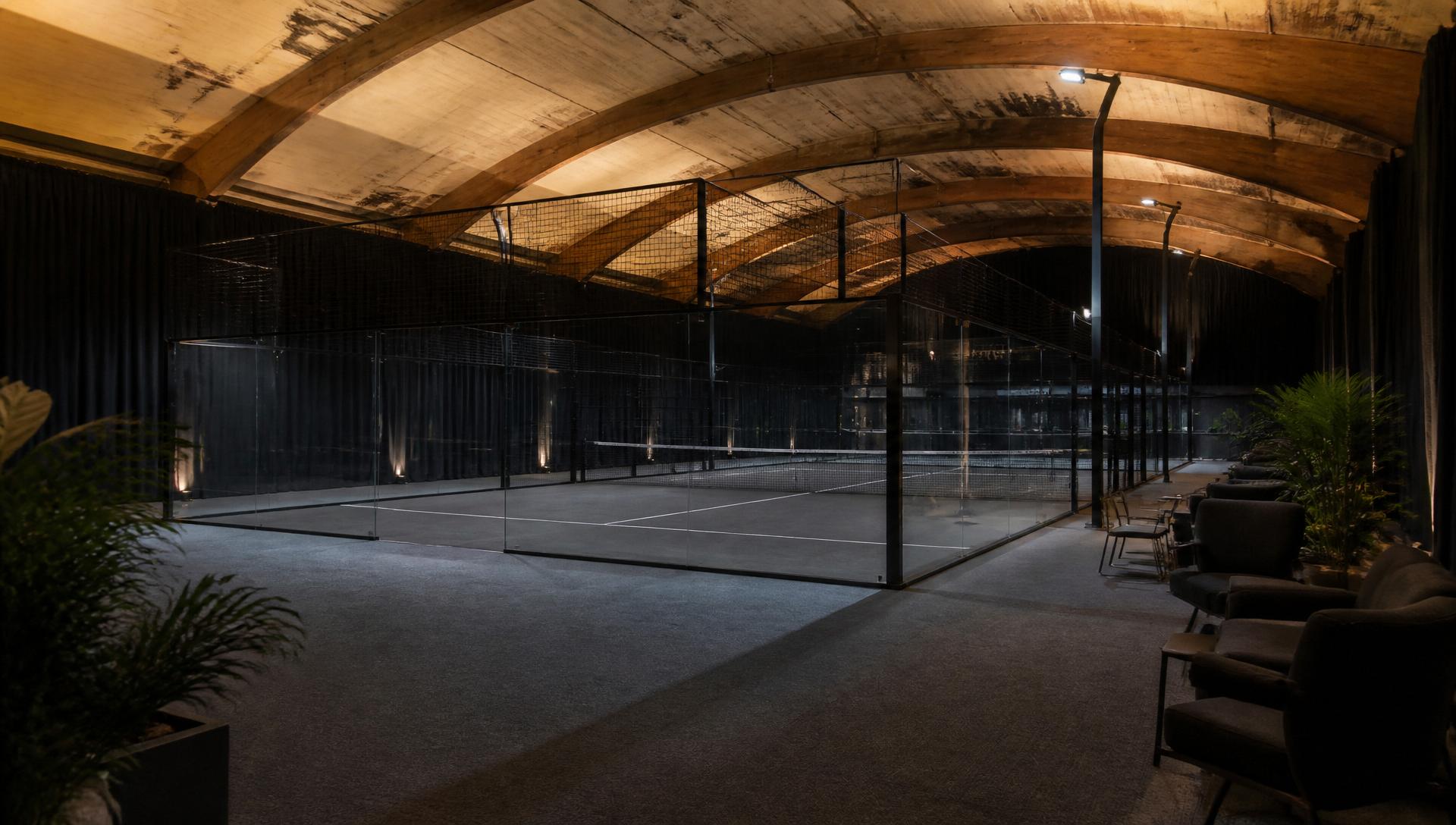 Dunkle Padelhalle in ehemaliger Tennishalle mit anthrazitfarbenem Boden und warmer indirekter Beleuchtung